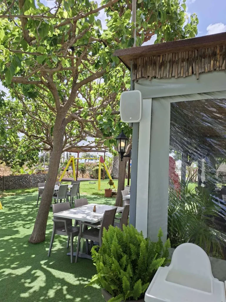 Discreet outdoor speaker on a wooden post in the garden seating at S.K. Yiallos